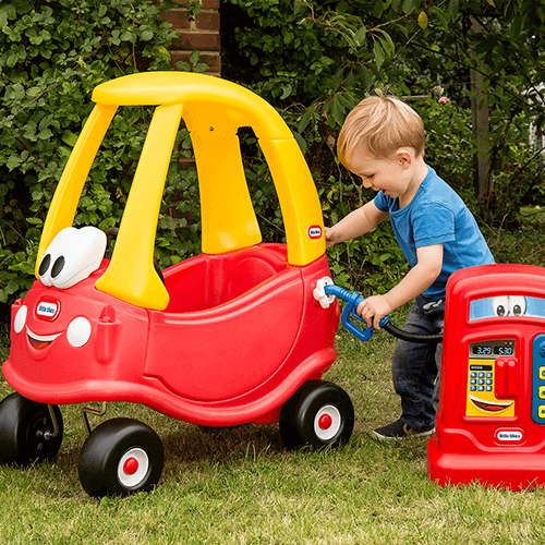 A happy little boy pretending to fill up a little tikes buggy with gas from the little tikes gas pump